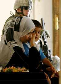 Una iraquí y su hijo esperan mientras su vivienda es inspeccionada por soldados estadunidenses, en Bagdad