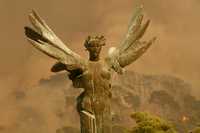 La estatua de la Victoria Alada destaca frente a una columna de humo provocada por un incendio en los alrededores de la antigua Olimpia, en el suroeste de Grecia, cerca de donde se realizaron los primeros Juegos Olímpicos