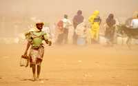 Una joven lucha contra el viento durante una tormenta de arena en un campo para refugiados de Darfur, en Sudán