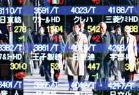 Trabajadores japoneses ante el reflejo de un tablero con los precios de las acciones bursátiles, a mediados de mes en Tokio