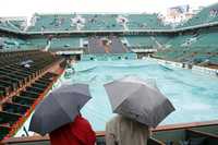 Asistentes al Roland Garros se protegen de la incensante lluvia que obligó a suspender varios partidos