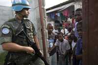 Un miembro de la fuerza internacional de paz de la ONU vigila junto a niños haitianos que esperan alimentos ante una escuela, el mes pasado en Puerto Príncipe