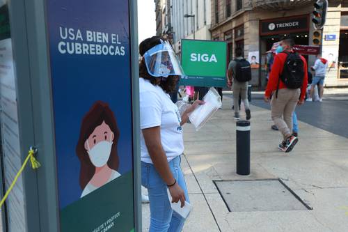 En busca de disminuir contagios, trabajadora del gobierno de la CDMX ofrece gel antibacterial y cubrebocas a quienes circulan por la calle Madero, en el Centro Histórico, donde en estos días se aglomera mucha gente.