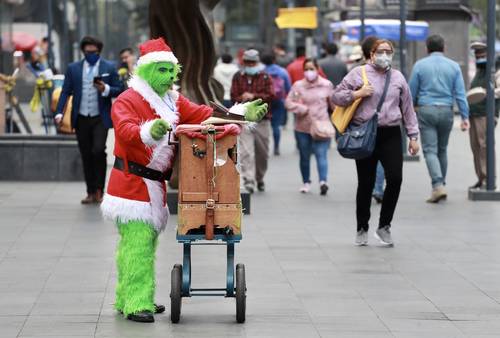 Un organillero disfrazadode Santaclós grinch toca su instrumento en la avenida Juárez, en el Centro Histórico, en medio del ir y venir de transeúntes que laboran o sólo visitan la zona.