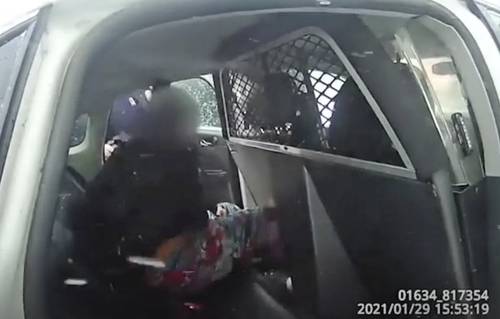 En imagen del 29 de enero tomada de un video de la cámara que llevan en el uniforme agentes de policía, una niña de nueve años bajo custodia es subida esposada a una patrulla después de que le lanzaron gas pimienta mientras gritaba llamando a su padre.