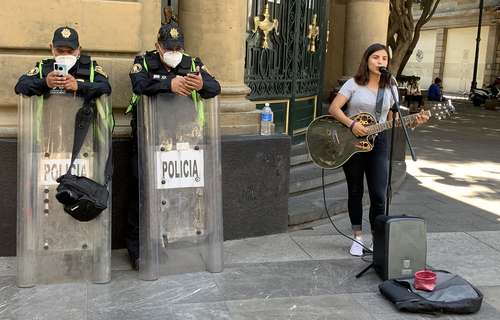 En la calle Venustiano Carranza en el Centro Histórico, una cantante comparte banqueta con granaderos ocupados en su celular, mientras cursa el mes 10 de la pandemia y la Ciudad de México se encuentra en semáforo de máxima alerta epidemiológica.