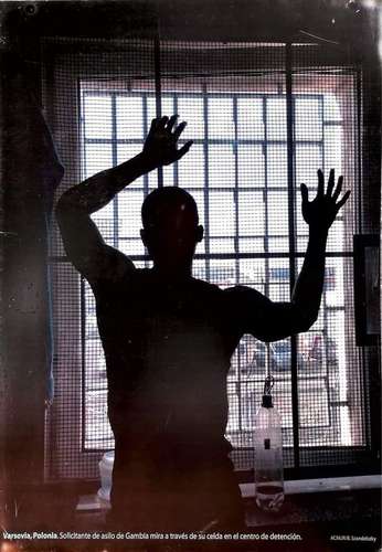 En esta imagen incluida en la exposición, un solicitante de asilo de Gambia mira a través de una ventana en un centro de detención en Varsovia, Polonia.