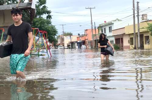 Vecinos del fraccionamiento Los Sauces, en Matamoros, caminan en calles inundadas debido a las torrenciales lluvias.