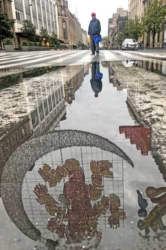 Tras la lluvia de ayer por la tarde, un hombre, parado a media calle, admira uno de los mosaicos luminosos con motivos prehispánicos instalados en el Centro Histórico de la Ciudad de México.