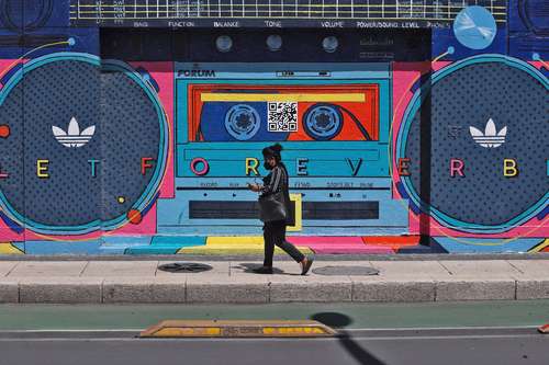 Una mujer camina ensimismada con su teléfono celular frente a un grafiti de una grabadora ochentera sobre Paseo de la Reforma.