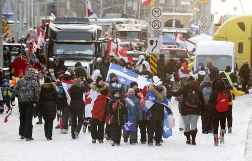 Habitantes de Ottawa caminan entre los camiones que bloquean calles del centro de la capital canadiense en protesta por las restricciones para contener el covid.
