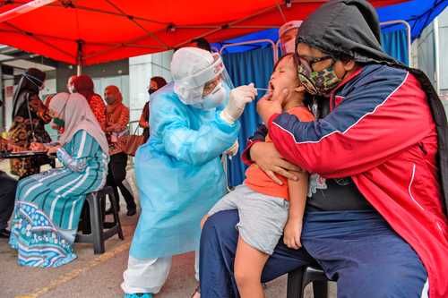  El debate por la atención a las contagios por covid-19 en los niños va en aumento. En la imagen, un empleado médico toma una muestra salival a un pequeño en la localidad de Shah Alam, Selangor, Malasia. Foto Xinhua