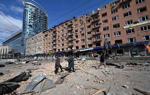  Civiles caminan al lado de edificios destruidos de la capital ucrania, que se encuentra bajo asedio del ejército ruso. Foto Afp
