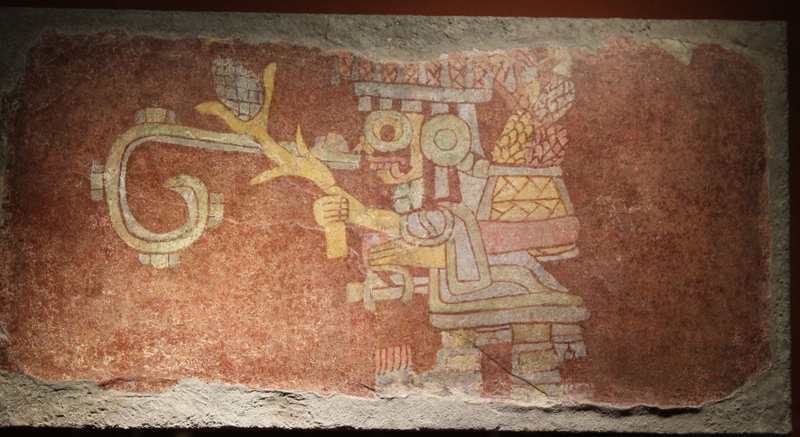 Tláloc, el dios del agua y de la fertilidad, lleva un canasto con mazorcas de maíz y sostiene una planta de maíz y una bolsa en sus manos