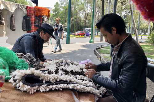 Ofelio Flores, originario del estado de Hidalgo, y Samuel González López, de Puebla, elaboran un tapete artesanal con lana hilada de borrego. El artículo, que les lleva unos 15 días terminarlo, tiene un valor de 3 mil 200 pesos.
