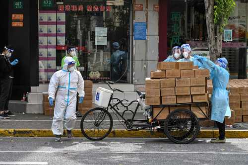 Trabajadores de servicio de entrega de paquetería portan trajes de protección durante sus labores en una de las zonas en cuarentena por el covid-19 en Shanghai, China.