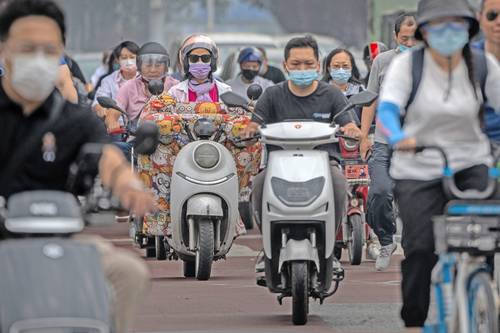 Aun al aire libre, viajeros en moto o bici portan cubrebocas en el distrito de negocios de Pekín, capital de China.