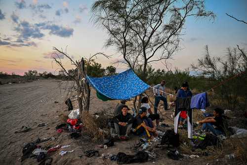 Personas que acaban de atravesar el río Bravo descansan en lo que esperan ser aprehendidos por la Patrulla Fronteriza, en Eagle Pass, Texas.