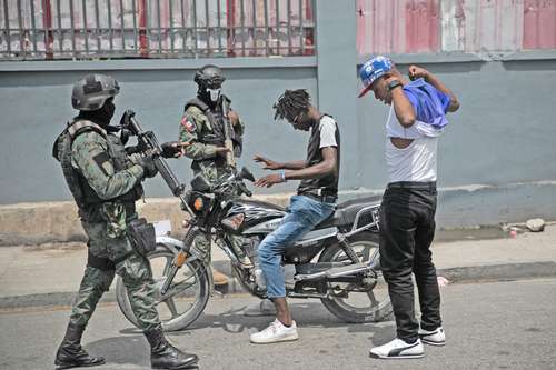 Elementos de las fuerzas armadas revisan, en busca de armas, a dos hombres que conducían una motocicleta ayer, en el área de las oficinas estatales de Puerto Príncipe.