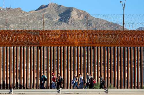 Indocumentados provenientes de Venezuela caminan al lado del muro en El Paso, Texas, luego de cruzar el río Bravo desde México y antes de entregarse a la Patrulla Fronteriza.