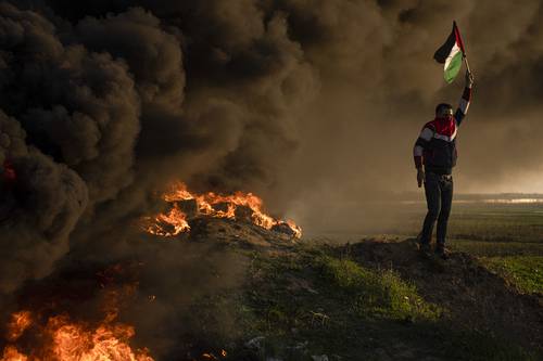 Palestinos queman neumáticos y ondean la bandera nacional durante una protesta contra el ataque militar israelí en la ciudad cisjordana de Jenin, a lo largo de la valla fronteriza con Israel.