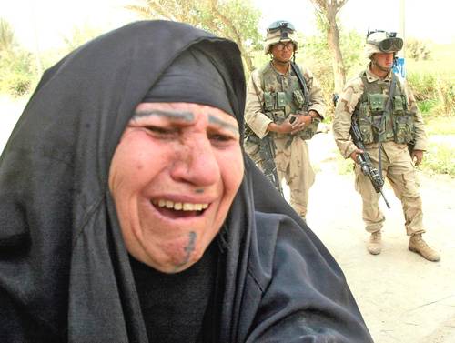 En imagen del 12 de abril de 2003, una mujer iraquí llora porque no puede encontrar a sus dos hijos en el hospital siquiátrico de Bagdad, mientras dos infantes de marina montan guardia en el fondo. A 20 años de la invasión a Irak liderada por Estados Unidos que derrocó a Saddam Hussein, el país rico en petróleo sigue marcado por el conflicto.