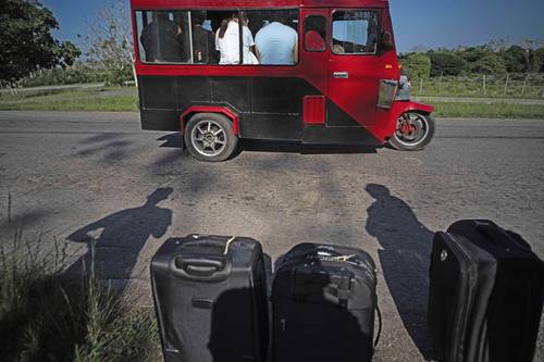 Personas con sus equipajes ven pasar este viernes un transporte lleno mientras esperan un taxi cerca de Catalina de Güines, Cuba. Debido a la escasez de combustible, el gobierno ha restringido la venta.