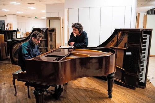 Tim Vincent-Smith escucha a un voluntario probar un piano en su taller en Edimburgo.