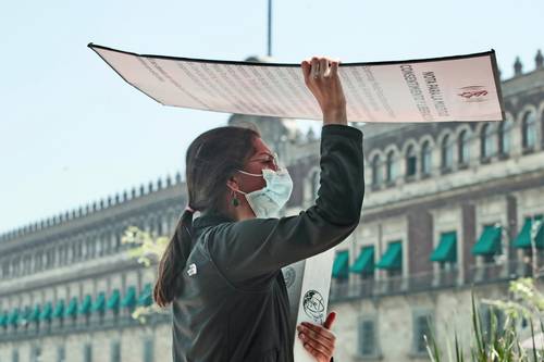 Una mujer aprovecha cartelones de una protesta afuera de Palacio Nacional para protegerse del sol.
