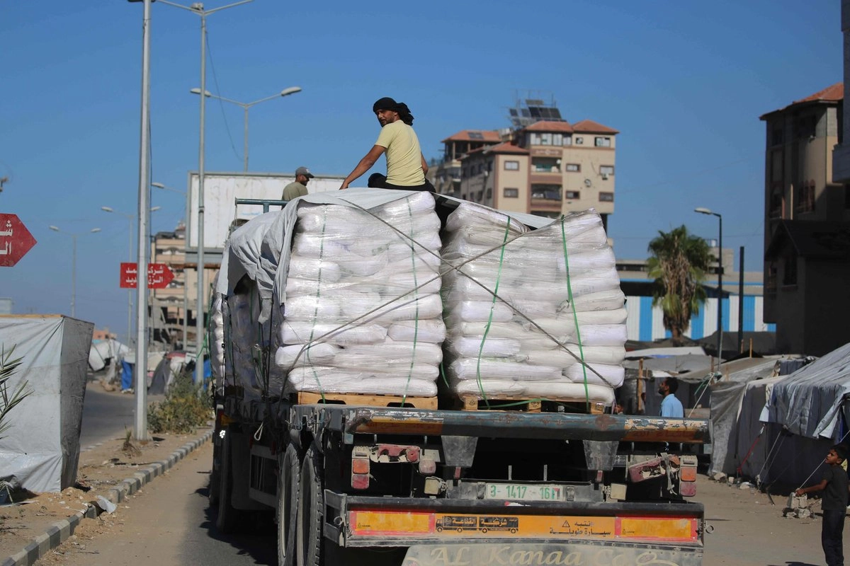 Camiones con ayuda humanitaria que entraron en la Franja de Gaza por el cruce de Karm Abu Salem pasan junto a las tiendas de campaña para desplazados en el campo de refugiados de Nuseirat, en el centro de la Franja de Gaza, el 14 de octubre de 2025, un día después de la entrada en vigor del alto el fuego entre Israel y las facciones palestinas. Foto