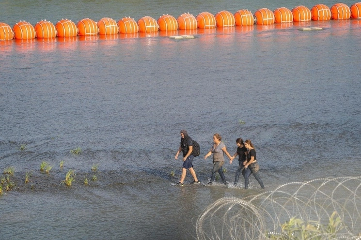 Migrantes caminan cerca del muro de boyas colocado a lo largo de la frontera de Río Grande con México, el 16 de julio de 2023. Foto Afp