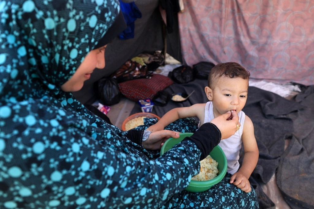 Una mujer alimenta a un bebé con bebé de ayuda humanitaria, en un campo para desplazados al sur de la Franja de Gaza. Foto Afp