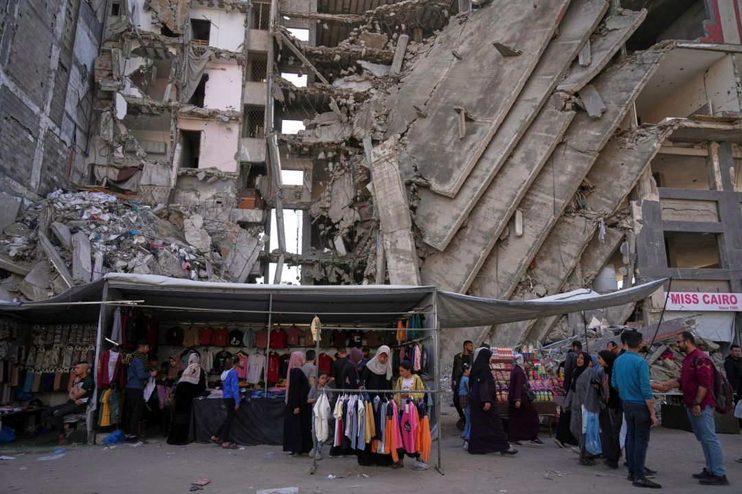 Palestinos compran ropa en una tienda junto a un edificio de apartamentos destruido en preparación para las celebraciones del Eid al-Adha en el barrio de Al-Rimal en el centro de la ciudad de Gaza el viernes 28 de marzo de 2025.