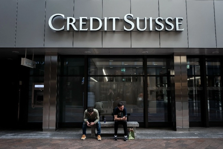 Dos hombres se sientan bajo un cartel de Credit Suisse que se muestra en un edificio en Lugano, Suiza. Foto Afp