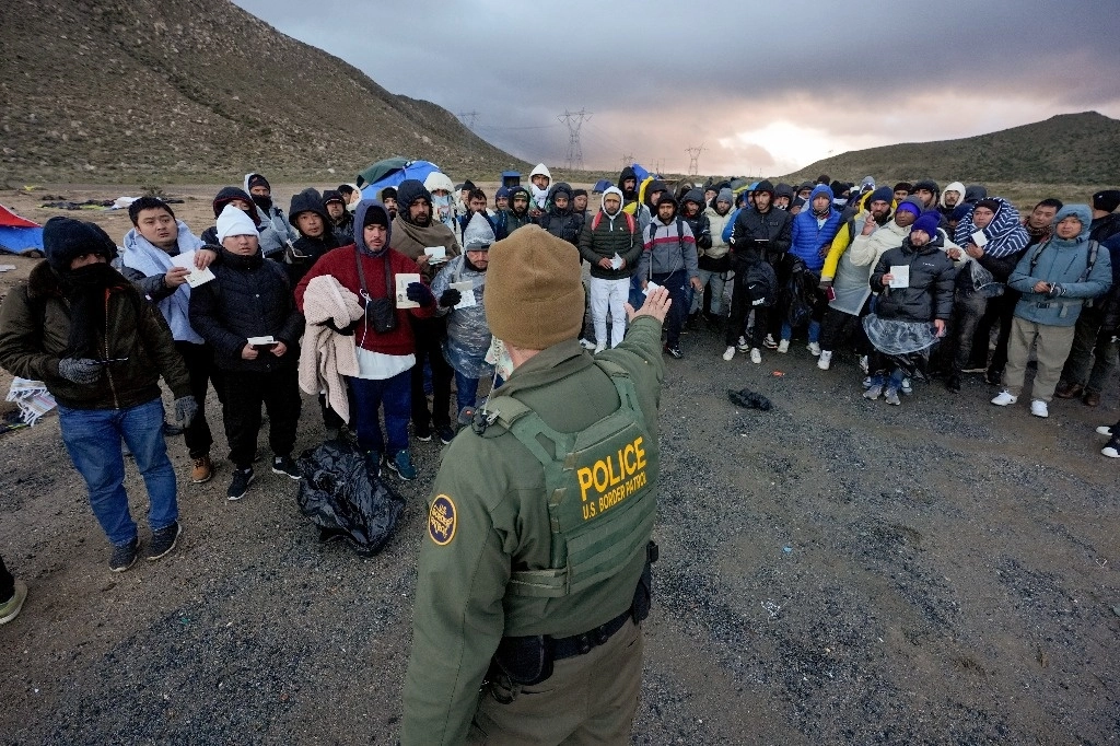 Un agente de la Patrulla Fronteriza pide a los migrantes solicitantes de asilo que hagan fila en un campamento montañoso improvisado después de que el grupo cruzó la frontera con México, el viernes 2 de febrero de 2024, cerca de Jacumba Hot Springs, California. Foto Ap