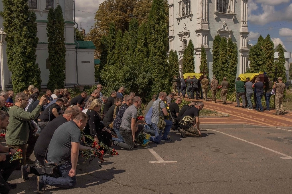 Los dolientes se arrodillan para presentar sus respetos mientras los hombres cargan ataúdes durante el funeral de seis militares ucranianos, que murieron desde que Ucrania lanzó su ofensiva en la región fronteriza rusa de Kursk, en Sumy, noreste de Ucrania, el 15 de agosto de 2024. Foto Afp