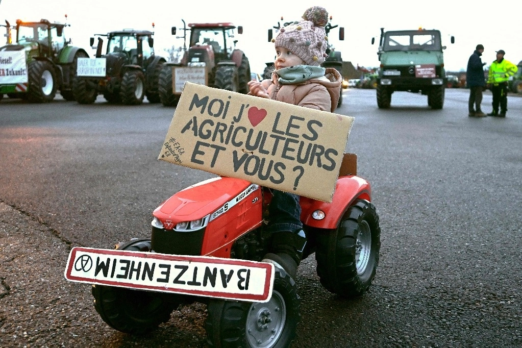 La hija de un granjero en un tractor para niños, con una pancarta en la que se lee “Yo amo a los agricultores, ¿y tú?", durante una protesta en la frontera franco-germana en Ottmarhsiem, al este de Francia, el 1 de febrero de 2023. Foto Afp 