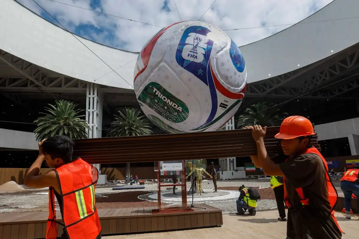 Trabajadores pasan frente a la versión gigante del balón Trionda, realizada por el mexicano Édgar Palafox y que fue colocada en el AICM con motivo del Mundial de futbol del próximo año. Foto