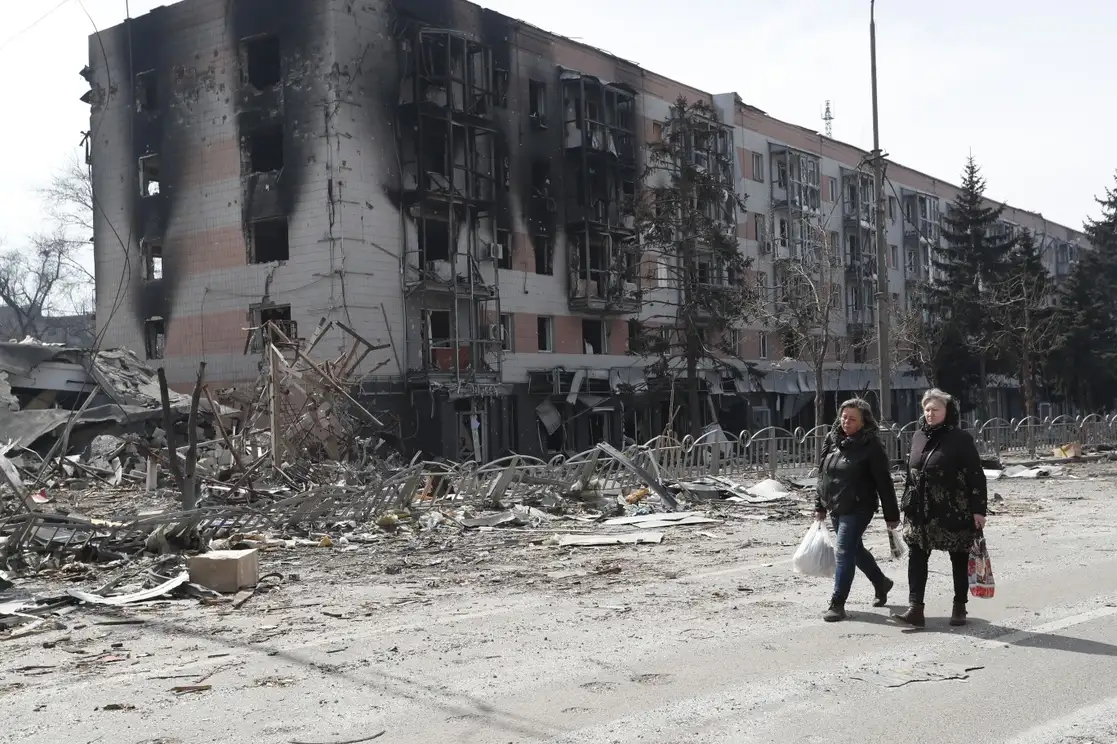 Dos mujeres caminan junto a un edificio dañado en Mariúpol, el 10 de abril de 2022. Foto Xinhua