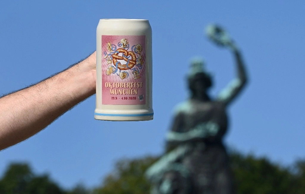 Un hombre sostiene un tarro oficial del Oktoberfest 2020 frente al monumento de Baviera, en Múnich, donde se realizaría el festejo anual de la cerveza. Foto Afp