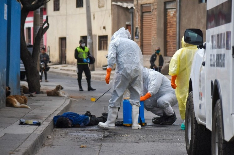Como parte del protocolo, trabajadores de salud desinfectan el cuerpo de un vendedor ambulante que fue encontrado al amanecer por sus vecinos en el barrio Cerro San Miguel de Cochabamba, Bolivia. El país suma 2 mil 535 decesos por Covid-19. Foto Ap