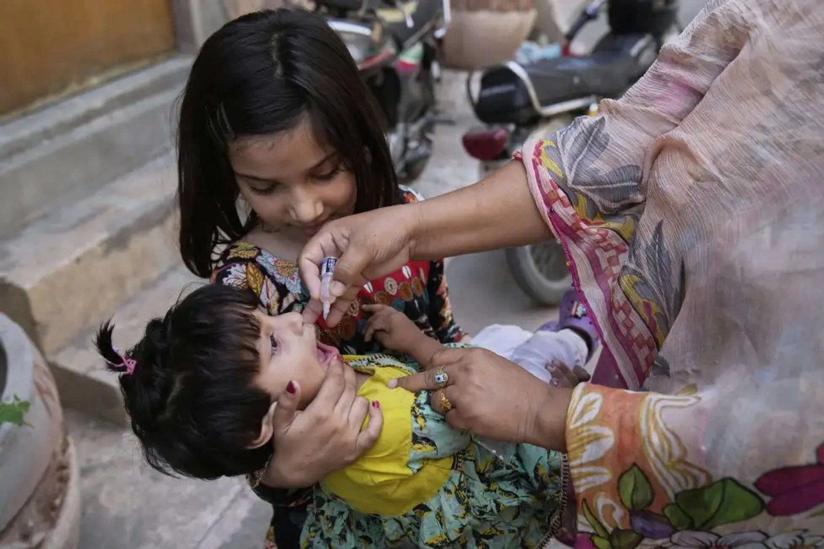Una trabajadora de salud administra una vacuna contra la polio a una niña en un vecindario en en Lahore, Pakistán.

