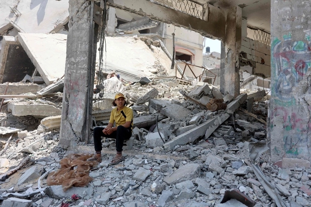 Joven palestino se cubre del sol a la sombra de edificios destruidos en el campamento de refugiados de Jabaliya, el 3 de junio de 2024. Foto Afp   