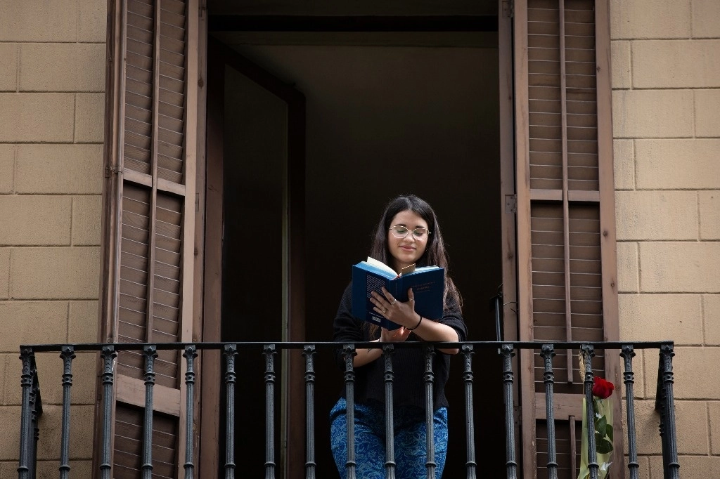 Una joven lee en un balcón en ocasión del Día de Sant Jordi, en el que es costumbre regalar libros y rosas en Barcelona. Foto Europa Press



