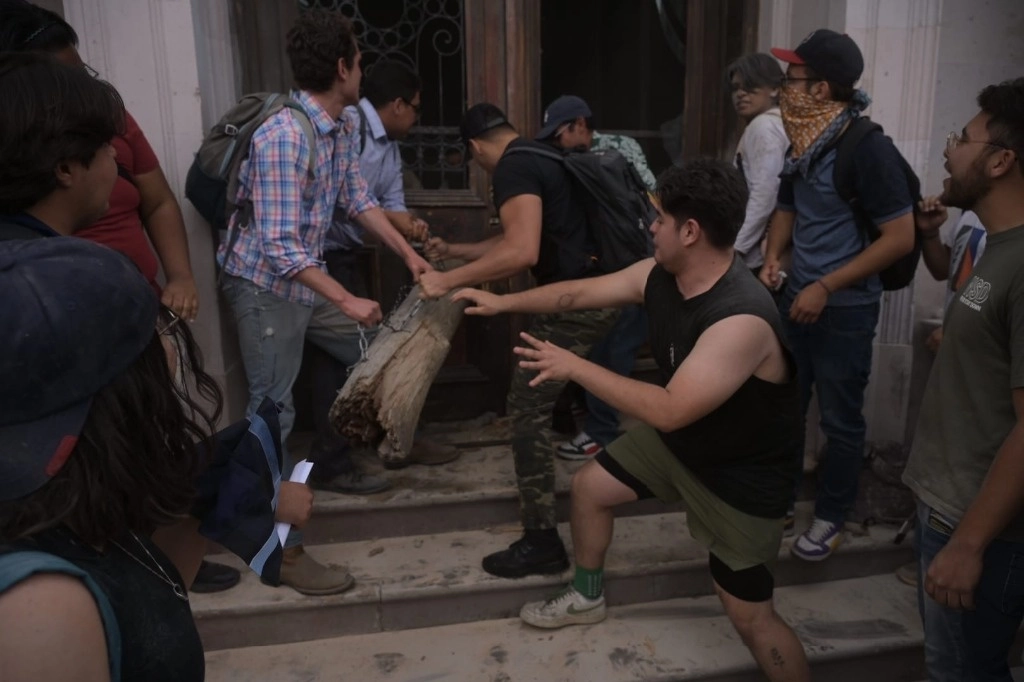 Estudiantes de la UACh usaron un tronco para derribar la puerta principal de la Rectoría de la UACh. Foto Cortesía Raúl Fernando Pérez-Raíchali