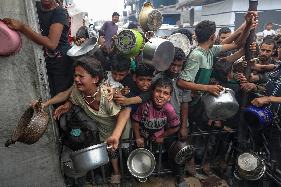 Niños palestinos se agolpan frente a un enrejado para recibir comida en un centro de distribución de alimentos, en la ciudad de Gaza.