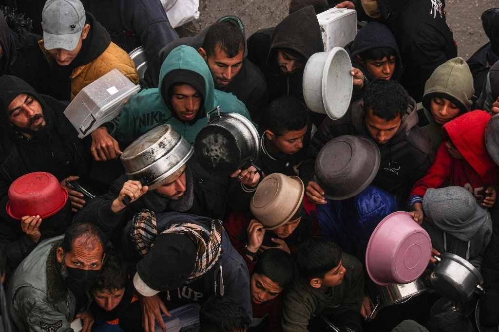 Los palestinos reciben raciones de alimentos en un centro de donación de un campamento para desplazados en Rafá. Esta ciudad ha tenido un enorme aumento de población en los cuatro meses pasados, a medida que los residentes se han trasladado lo más al sur posible. Israel amenaza ir sobre esta área, lo que ha agravado la zozobra. Foto Afp