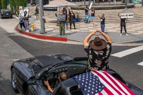 Manifestantes de Black Lives Matter levantan el puño al paso de una caravana en respaldo al presidente Donald Trump ayer en un vecindario de Los Ángeles. Foto Afp