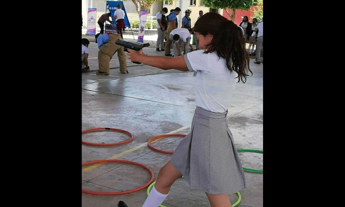 Una alumna de la secundaria técnica 54 “Mariano Matamoros”, en el municipio de Purísima del Rincón, manipula un arma de fuego durante una plática sobre prevención de adicciones impartida por policías municipales el 7 de julio. Foto tomada de Facebook