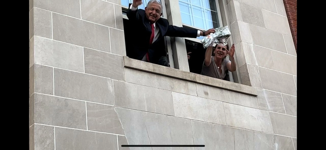 El presidente López Obrador y su esposa saludan desde la ventana de su hotel a mexicanos que llegaron a saludarlo. Foto La Jornada